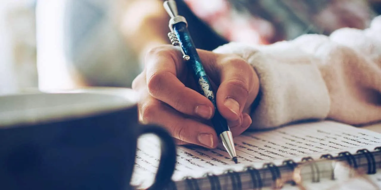 Close-up of a person writing in a notebook with a decorative pen, reflecting creativity and note-taking.