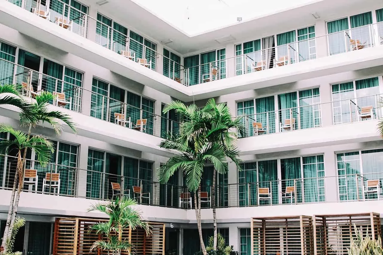 Luxury hotel building with multiple floors, glass balconies, and tropical palm trees for tropical vacation travel keyword opt