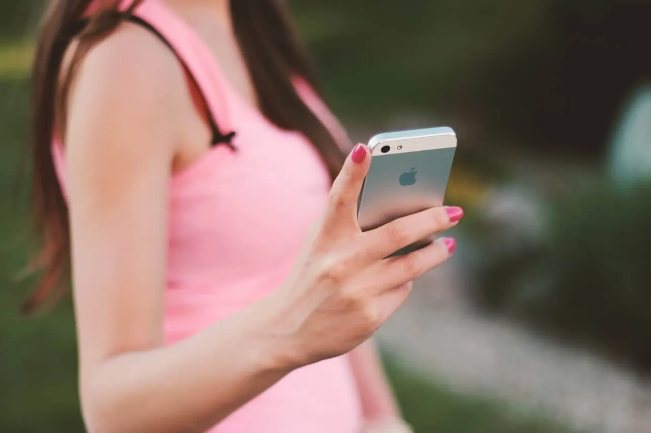 Iphone woman holding smartphone in outdoor setting, close-up of hand and device, pink dress, technology, mobile device, socia