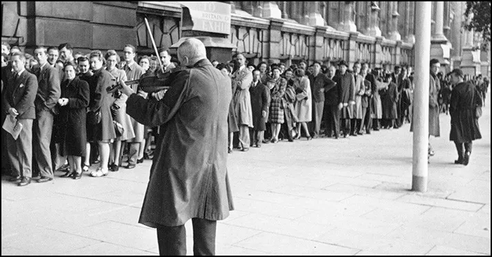 A long queue of people waiting outdoors in a city street, black and white vintage photo.