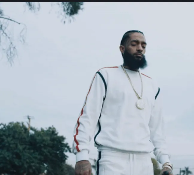 Stylish male rapper in urban streetwear with gold chain, outdoor setting, representing music and hip-hop culture for Hypebot'