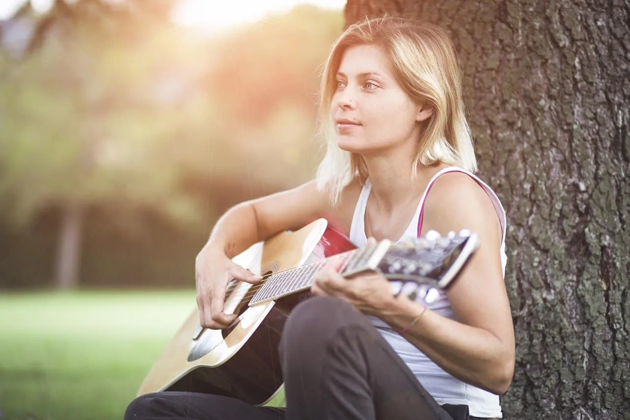 Girl playing acoustic guitar outdoors in park during sunset, relaxing and enjoying music, showcasing summer leisure, music th