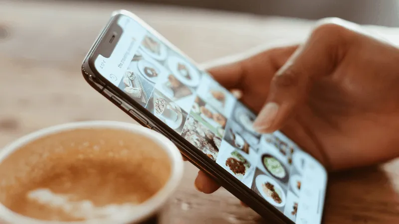 High-resolution smartphone displaying food images, coffee cup on wooden table, social media food photos, digital content crea