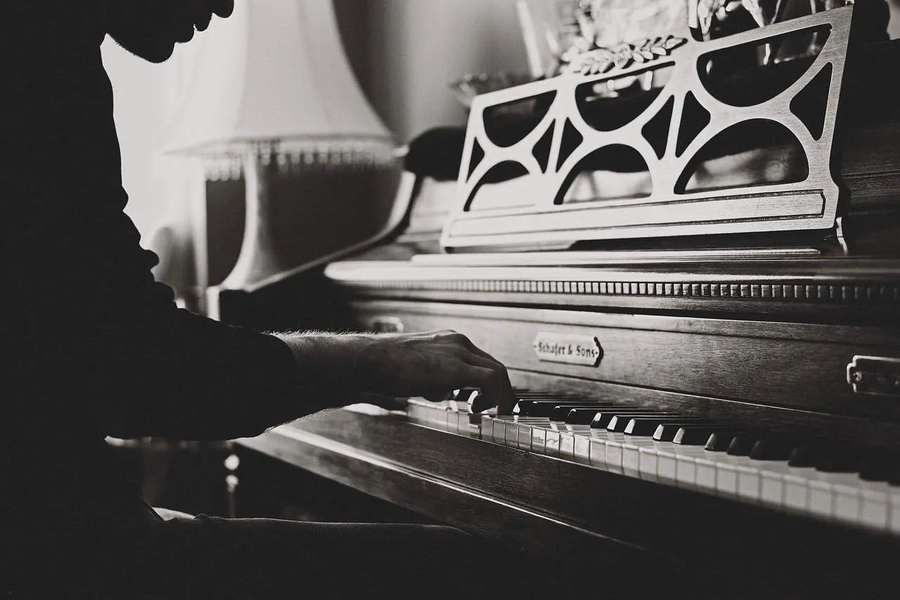 Piano player playing a classical Schwarzschild & Son upright piano in a cozy indoor setting, black and white photo emphasizin