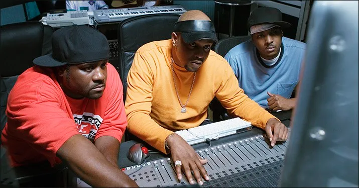 Professional music producers collaborating in a recording studio, using a mixing console and technology to create and mix mus