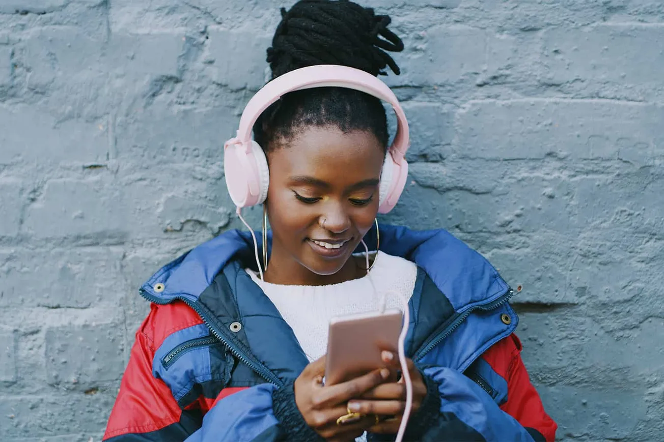 Young woman listening to music with pink headphones and smartphone against urban brick wall, enjoying music, urban lifestyle,