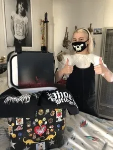 A woman wearing a face mask giving two thumbs up in a music studio with electronic equipment and a laptop.