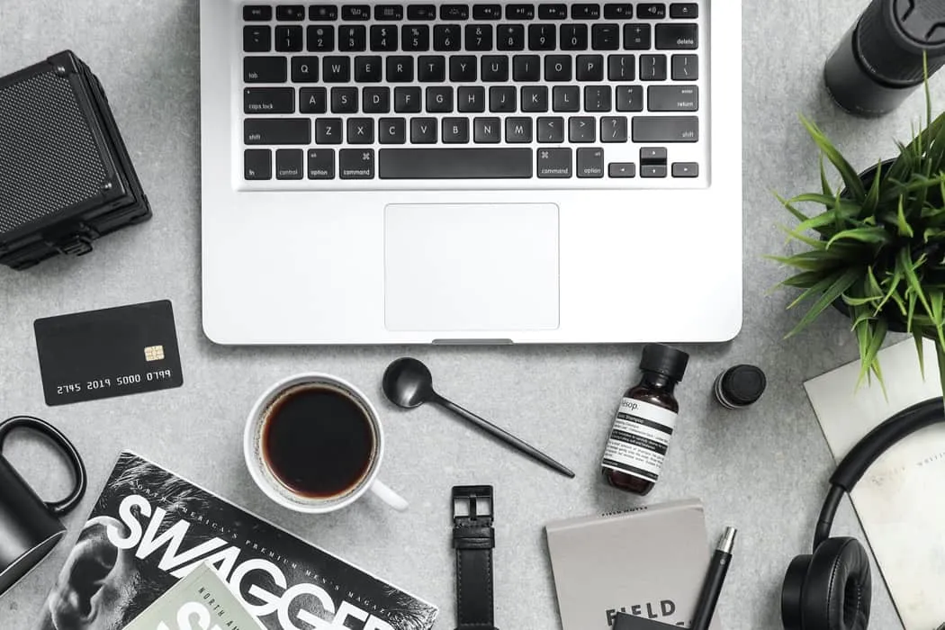 A flat lay of a workspace with a laptop, coffee, wearables, a credit card, and music gear, perfect for digital marketing, mus