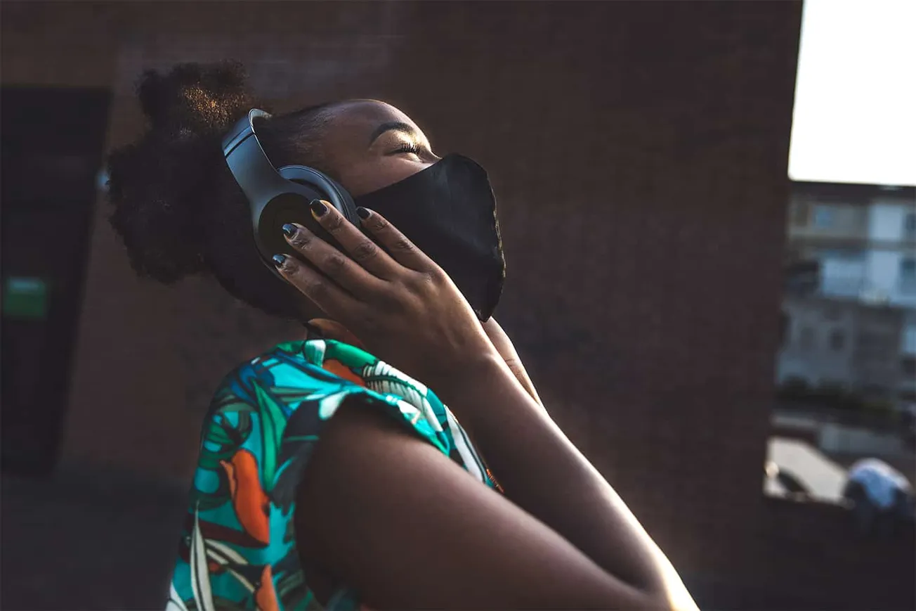 Young woman listening to music with headphones, wearing a face mask, in an urban environment, enjoying her favorite tunes, re