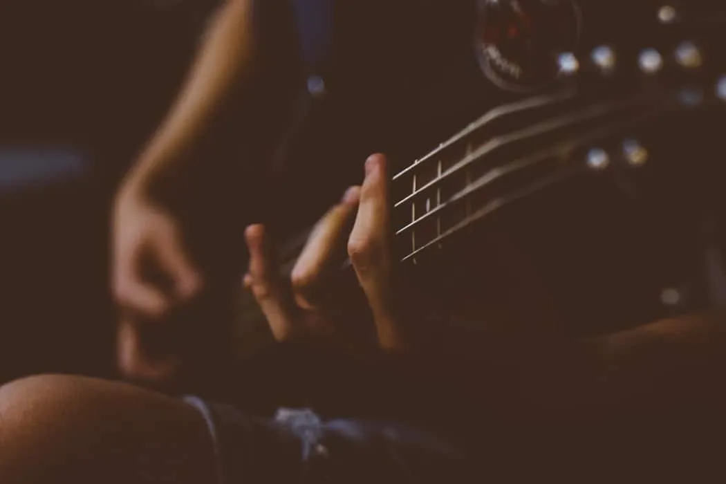 Close-up of musician's hand playing acoustic guitar, emphasizing music performance and artistry in a dimly lit setting.