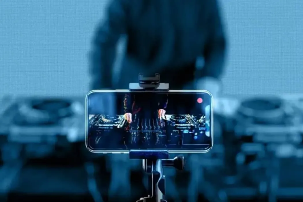 DJ mixing music in a club with live streaming on a smartphone for digital music promotion.
