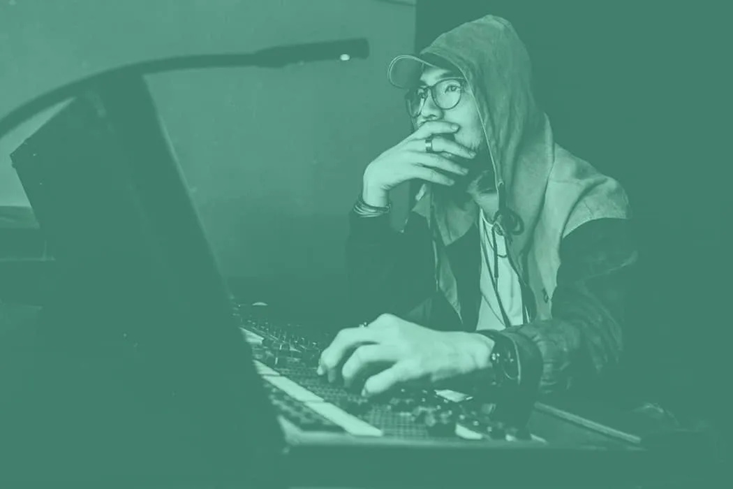 Young man working on music production, DJing, or audio editing at a computer with headphones and a hoodie, emphasizing digita