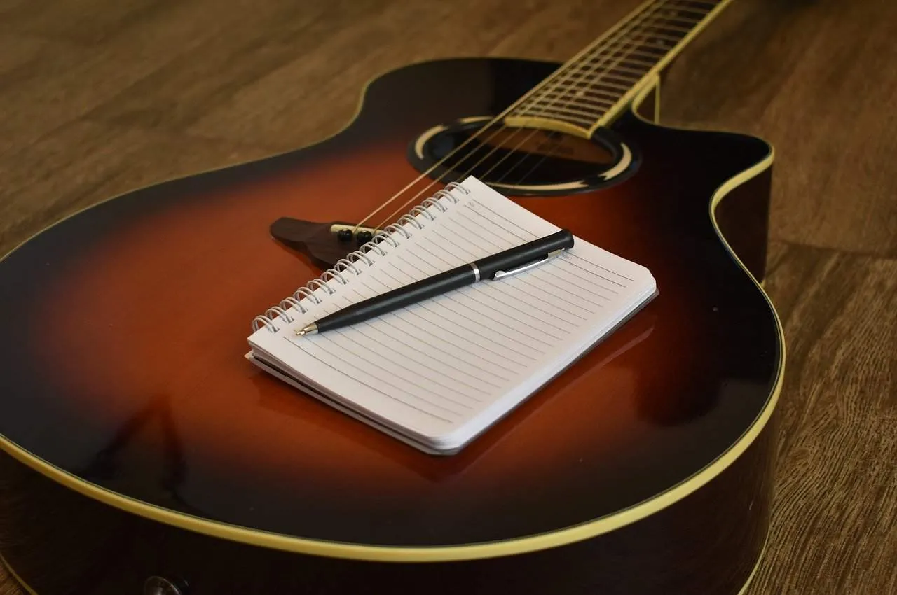A classic acoustic guitar with a notepad and pen resting on it, on a wooden floor, symbolizing music creation, songwriting, a