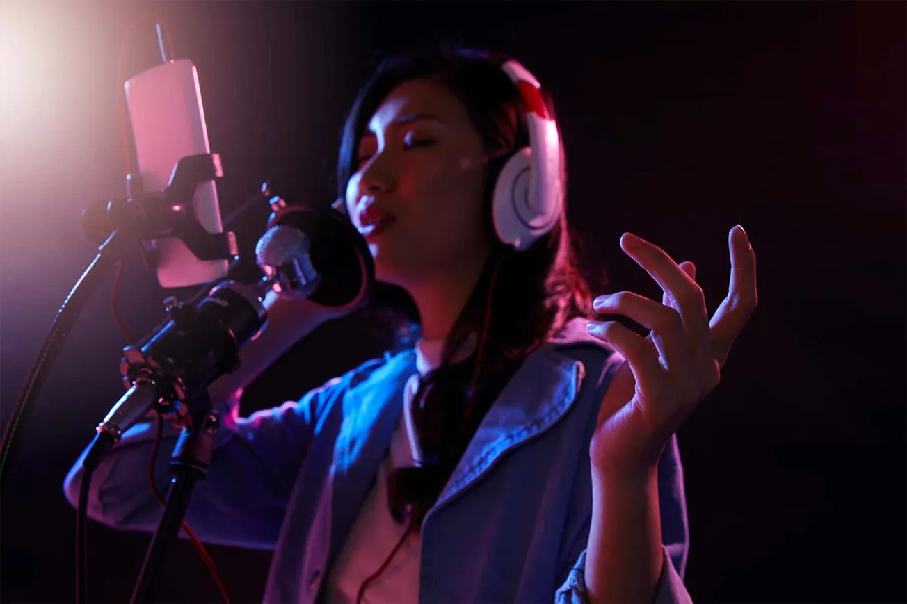 Professional female singer recording vocals in a dark studio with colorful lighting, wearing headphones and singing passionat
