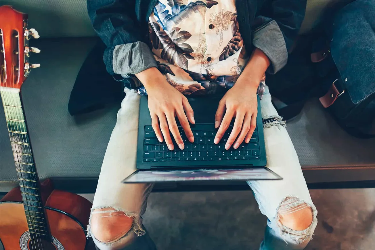 Guitar resting next to a person working on a laptop, casual music and technology workspace, creative music producer with acou