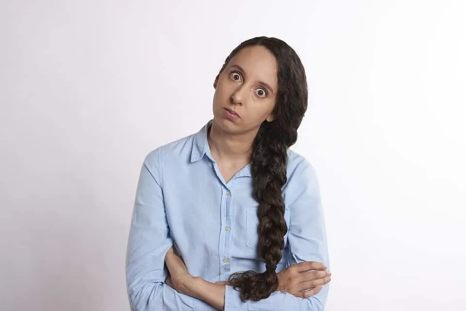 Confused woman with long braided hair wearing a light blue shirt, looking puzzled and confused, expressing uncertainty or cur