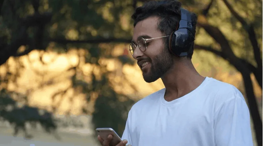 Young man listening to music with headphones outdoors, using smartphone, enjoying modern digital music, music technology, out