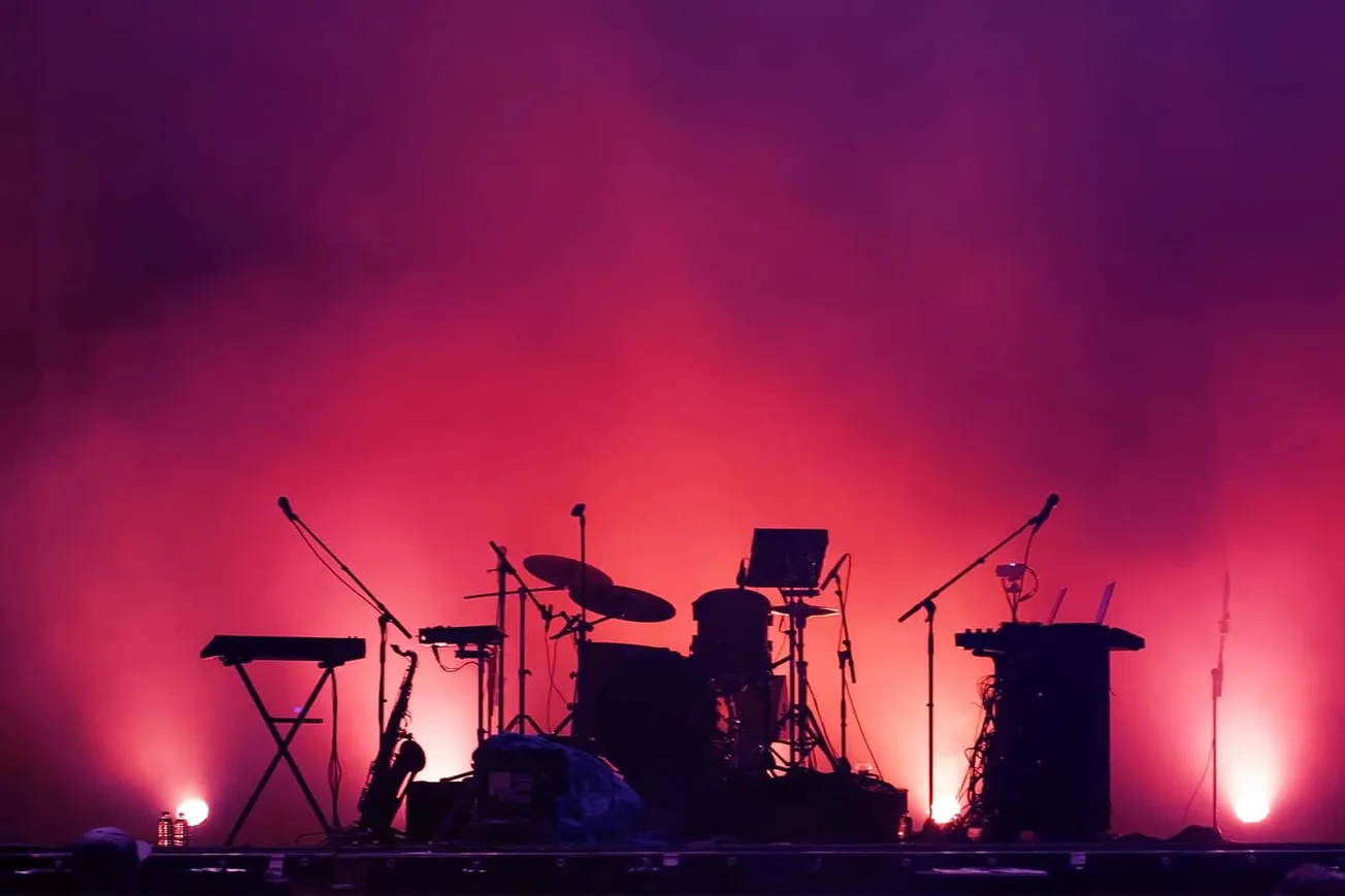 Vibrant concert stage setup with musical instruments illuminated by colorful pink and purple lighting, creating an energetic