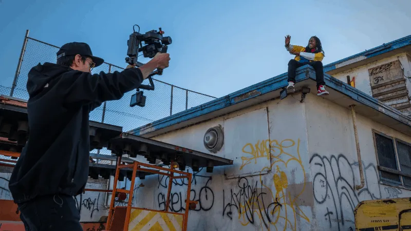 High-angle shot of a videographer filming a person sitting on a graffiti-covered rooftop during sunset, capturing urban cultu