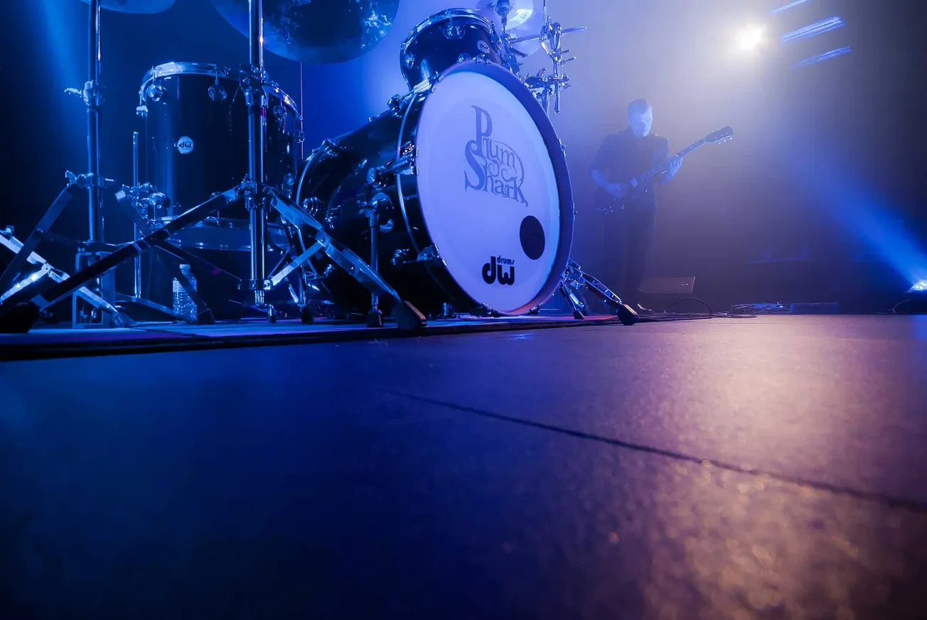 Vivid shot of a drum set featuring a bass drum with "Drum & Shank" logo, illuminated with dynamic blue and purple stage light