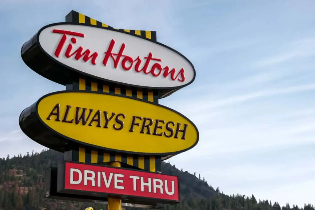 Tim Hortons fast-food restaurant drive-thru sign with "Always Fresh" slogan, outdoor setting with mountains in the background