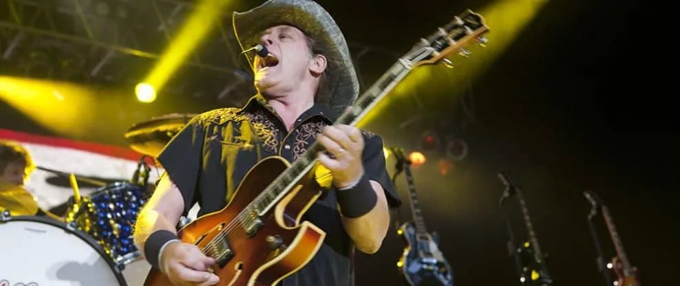 Energetic musician playing guitar on stage during a lively concert performance with colorful lighting effects.