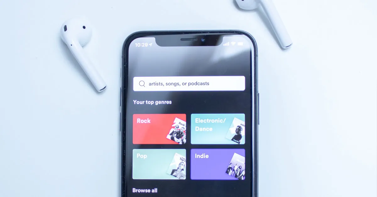 Music streaming app displaying top music genres on smartphone screen with wireless earbuds on a white surface alt text: moder