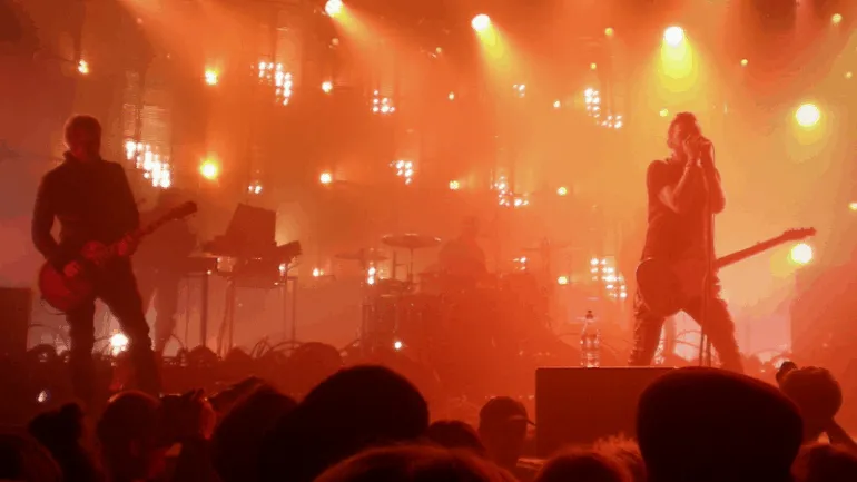 Electric guitarists and a vocalist performing live on stage at a concert with vibrant orange and yellow stage lighting, creat