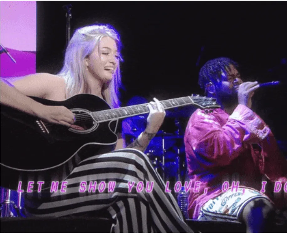 Playing acoustic guitar and singing into a microphone during a live music performance, with colorful stage lighting and overl