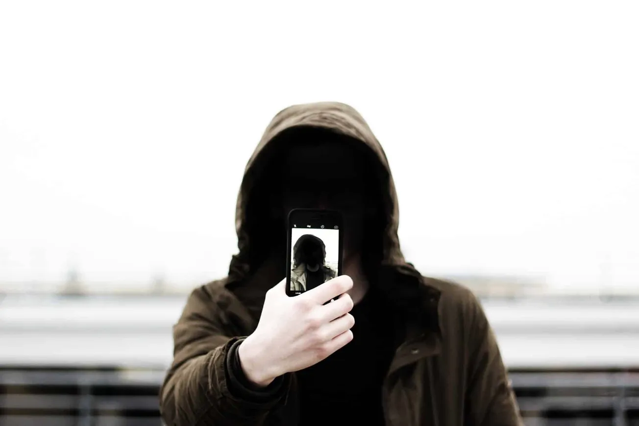 Hypebot music industry news, persona, and digital marketing concepts, person taking photo in hoodie with smartphone on bridge