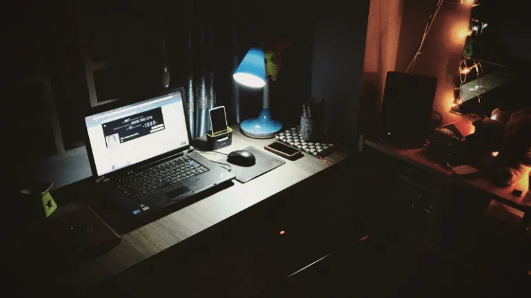 Laptop workspace at night with desk lamp, smartphone, and headphones, showcasing a creative home office setup ideal for digit