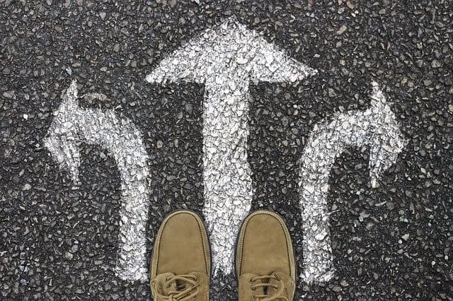 Uncertain path options with directional arrows painted on asphalt, viewed from a person's feet, symbolizing decision making a
