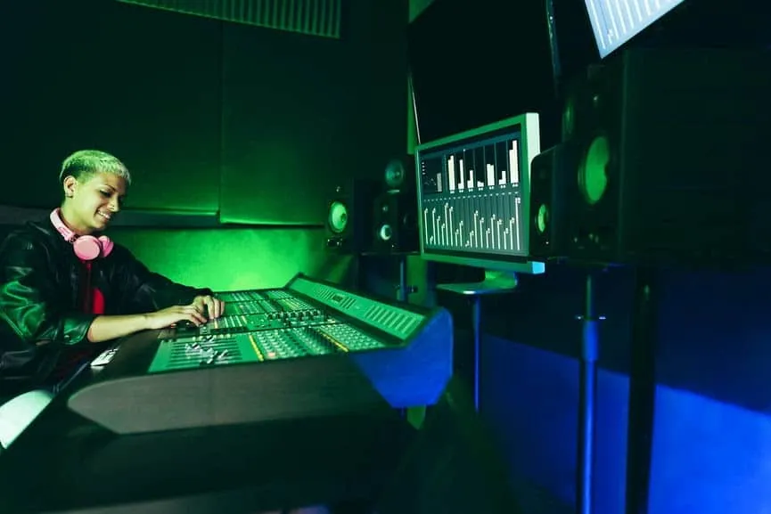 Boy operating music mixing console in a recording studio with visualizer screens, emphasizing music production, audio enginee