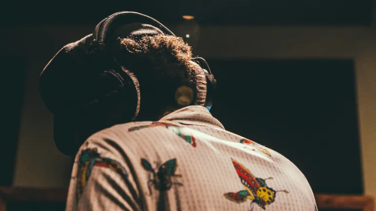 Headphones wearer in a recording studio wearing a floral and butterfly print shirt, focused on music production, representing