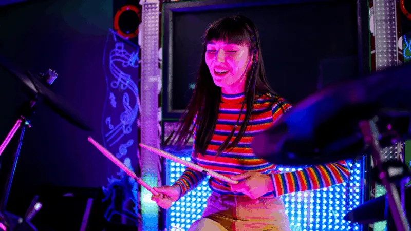 Drummer girl playing electronic drums at music venue with vibrant LED lights, live performance, modern music setup, colorful