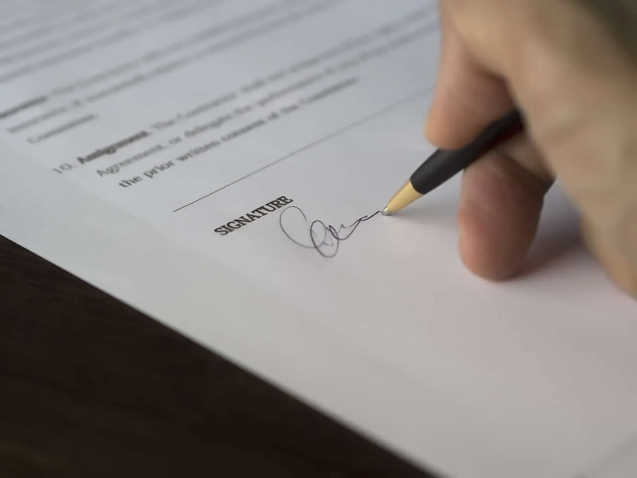 Signature being written on a document with a pen, representing legal or formal paperwork, contracts, or agreements.