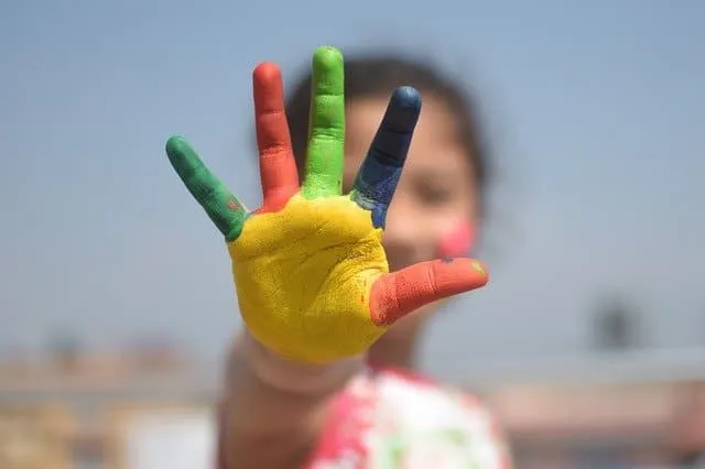 Colorful painted hand blocking the view of a child's face, highlighting themes of creativity and childhood.