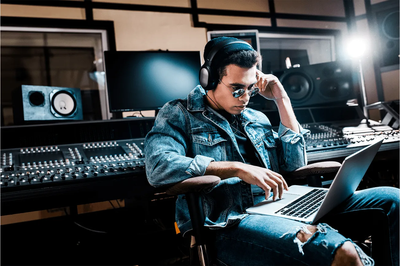 Young male music producer working in a professional recording studio with audio mixing equipment, headphones, and a laptop, f
