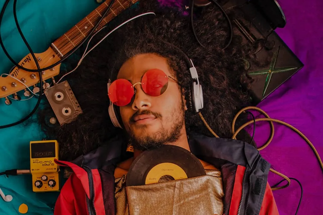 Creative musician lying on colorful background with headphones, vinyl, and musical equipment for music production and DJing S
