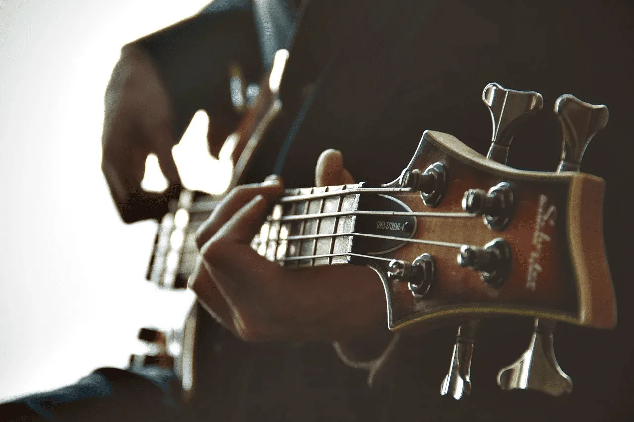 Guitarist playing electric bass guitar, close-up of hand on fretboard with tuning pegs visible, music, instruments, entertain