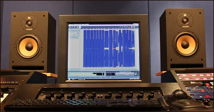 Studio music production equipment with computer monitor displaying audio editing software, professional sound mixing setup fo