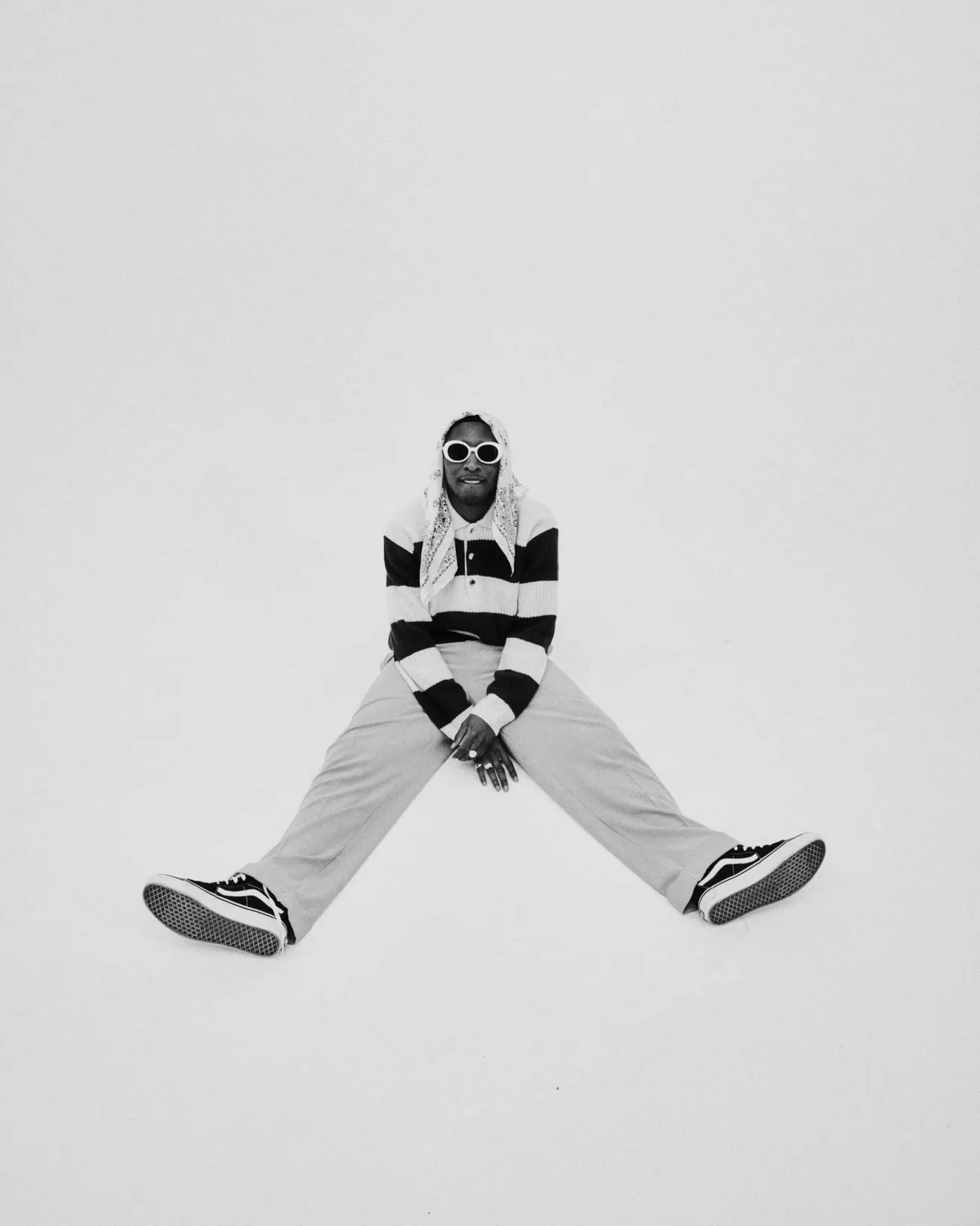 Stylish person in striped sweater, wide-leg pants, and sneakers, sitting on their side with legs apart, wearing large white s