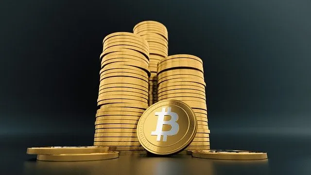 Stacks of gold Bitcoin coins with one prominently displayed front and center, representing cryptocurrency and digital finance