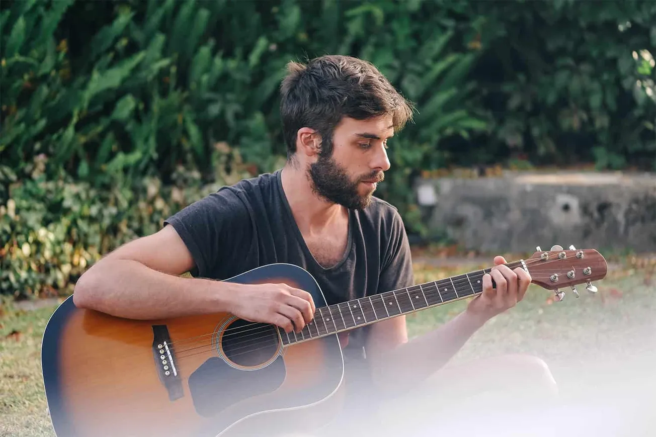 Young man playing acoustic guitar outdoors, relaxing in nature, soulful music, musician practice, outdoor guitar session, pea