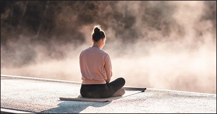 Person practicing meditation outdoors at sunrise or sunset, promoting mindfulness and wellness.