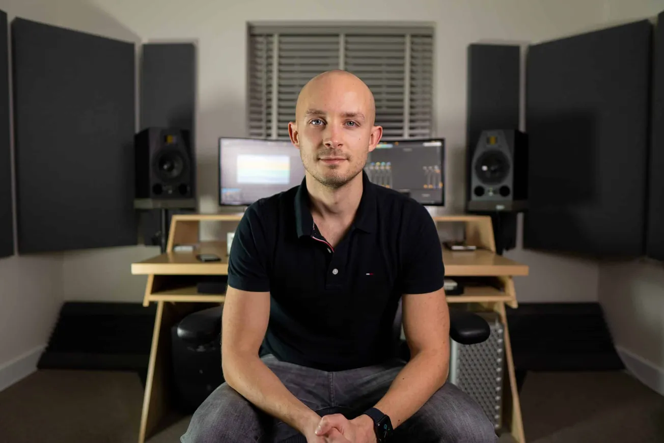 Bald man in music studio with professional sound equipment, mixing consoles, studio monitors, and acoustic panels, creating a