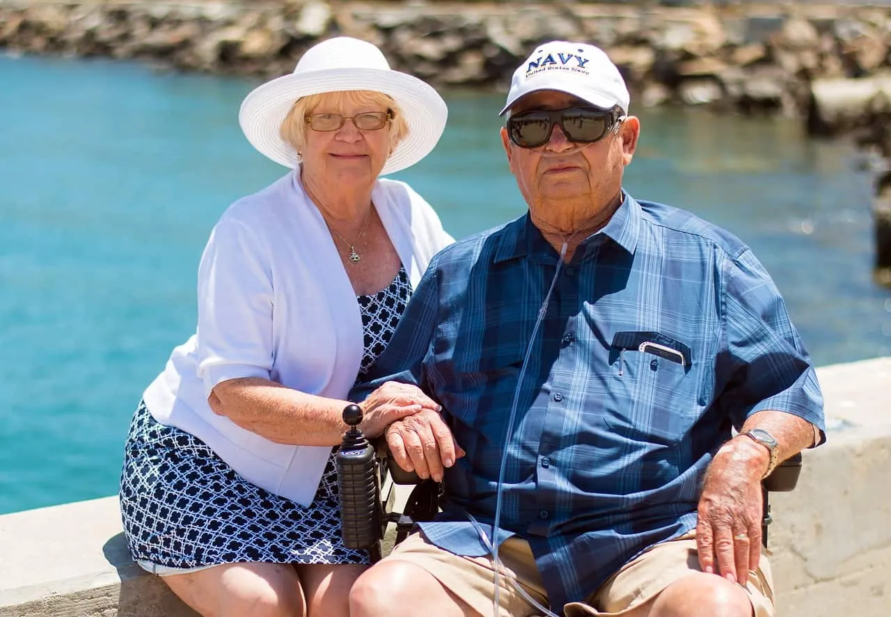 Enjoying retirement by the waterfront, senior couple with Navy veteran's hat, smiling and holding hands, sunny day, relaxing