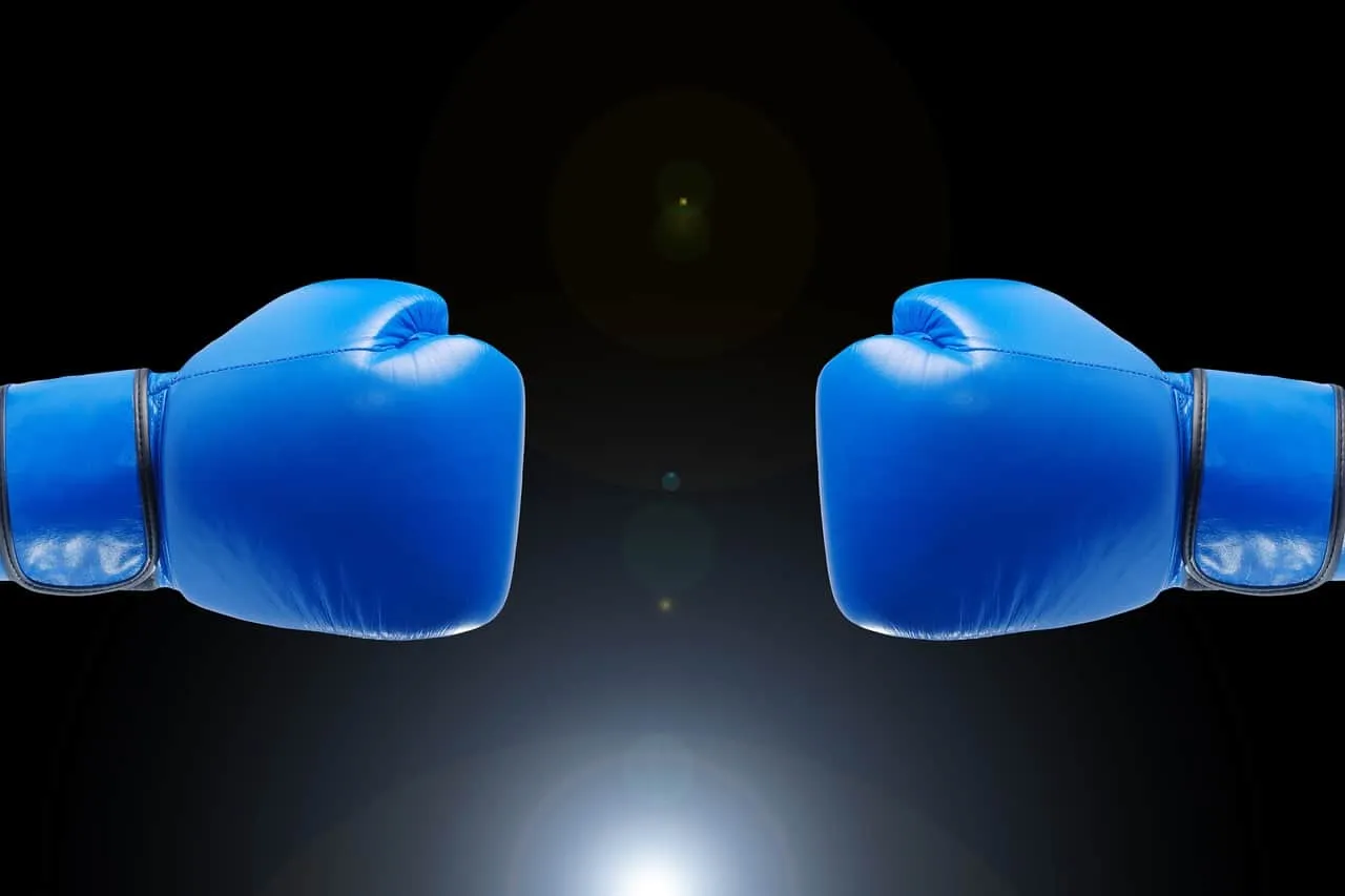 Blue boxing gloves facing each other against a black background, symbolizing competition or conflict, digital image related t