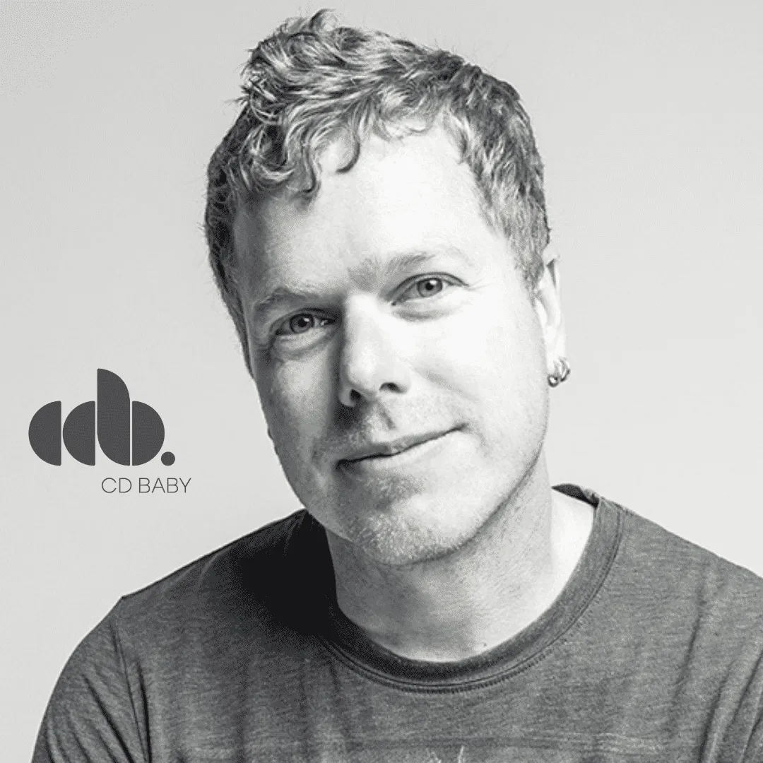Close-up photo of a young man with curly hair, wearing a casual t-shirt, smiling confidently. Black and white portrait emphas