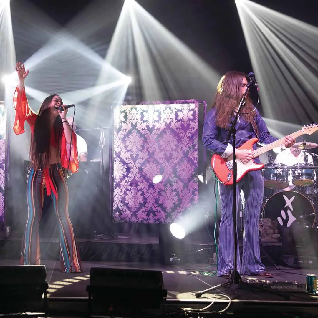 Performing indie pop band on stage with vibrant lighting, live music, and colorful stage design at a music concert.